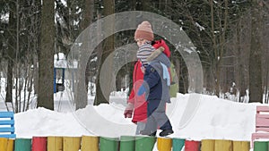 Cute little boy and young mother play in the winter with snow in the park. Blue kid`s jacket and red at mom.