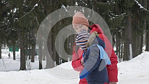 Cute little boy and young mother play in the winter with snow in the park. Blue kid`s jacket and red at mom.