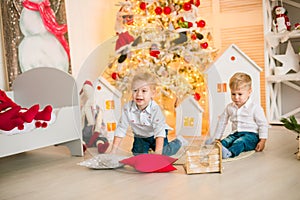 Cute little boys  with blond hair plays  in a bright room decorated with Christmas garlands near the Christmas tree.