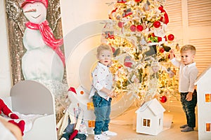 Cute little boys with blond hair plays in a bright room decorated with Christmas garlands near the Christmas tree.