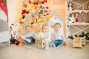Cute little boys with blond hair plays with little girl in a bright room decorated with Christmas garlands