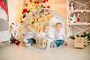 Cute little boys with blond hair plays with little girl in a bright room decorated with Christmas garlands