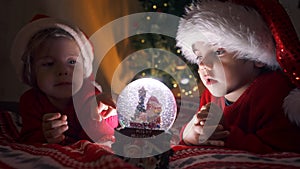 Cute little boys in Santa hats with snow globe. New Year's gift toy for children. Magic Christmas time, toddlers