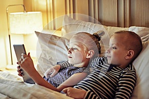 Cute little brother and sister lying in bed watching videos