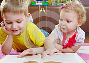 Cute little brother and sister reading book on floor