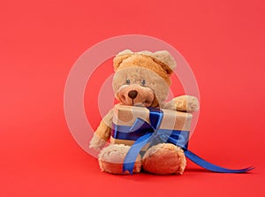 Cute little brown teddy bear holds a brown box with a blue ribbon