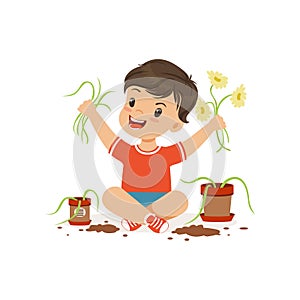 Cute little bully boy sitting on the floor and tearing flowers from pots, hoodlum cheerful little kid, bad child