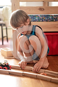 Cute little candid five year old kid boy playing at home with children`s toys cars and the wooden road on a floor of room in a co