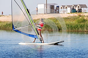 Cute little caucasian blond child girl enjoy having fun learning to surf on winsurfing board at freshwater pond lake or