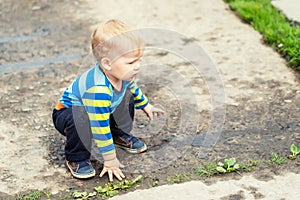 Cute little caucasian blond toddler boy having fun lying in a puddle after rain outdoors. Curious child discovering