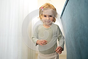 Cute little caucasian blonde baby girl of 1,2 years old playing games, running at home in light modern interior looking