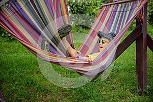 Cute little Caucasian boy relaxing and having fun in multicolored hammock in backyard or outdoor playground. Summer active leisure