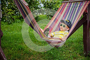 Cute little Caucasian boy relaxing and having fun in multicolored hammock in backyard or outdoor playground. Summer active leisure