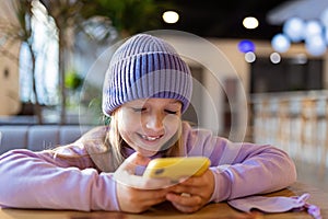 Cute little caucasian girl with blonde hair in trendy casual clothes using mobile phone in modern cafe at spring. Video