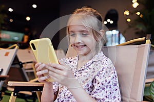 Cute little caucasian girl with blonde hair in trendy casual clothes using mobile phone in modern cafe at spring. Video