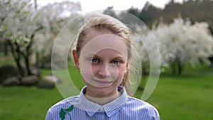 Cute little Caucasian girl with blue eyes in a beautiful shirt standing in the Park in springtime