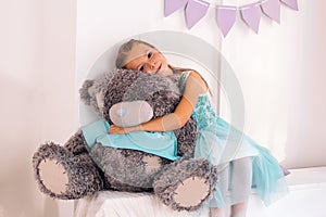 little caucasian girl hugs big gray teddy bear