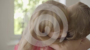 Cute little caucasian girl kissing caucasian woman on the cheek. Daughter hugging tight her mother with a long curly