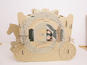 Cute Little Caucasian Girl in Pastel Pink Dress Princess Preparing for Birthday Party and posing in fairy tale carriage.
