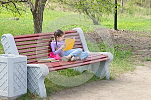 Cute little caucasian girl reading book sitting on a bench