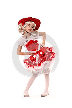 Cute little caucasian girl wearing red skirt, t-shirt with flowers and cowboy hat isolated on white background. She is dancing.