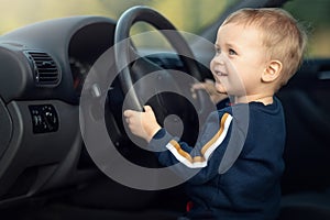 Cute little cheerful boy driving fathers car