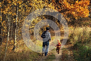 Cute little child boy and his father runs on a rural road in autumn forest. Time together dad and son outdoor in fall season. View