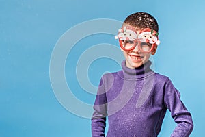 Cute little child boy in party Christmas Santa Claus glasses on blue background. Kid with snow on head copy space and