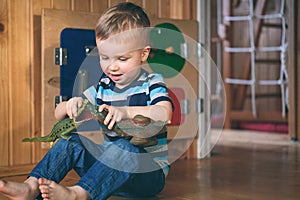 Cute little child boy playing with toy dinosaur and crocodile on busyboard background. Kid in kindergarten, nursery infant school