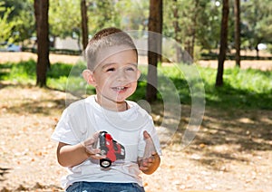 Cute little child boy plays with toy car in park on nature at summer.