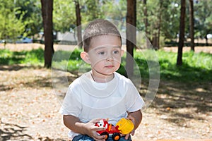 Cute little child boy plays with toy car in park on nature at summer.