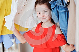 cute little child girl choosing new modern clothes in her wardrobe or store fitting room