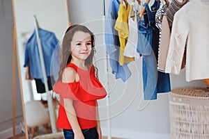 cute little child girl choosing new modern clothes in her wardrobe or store fitting room