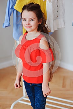 Cute little child girl choosing new modern clothes in her wardrobe or store fitting room