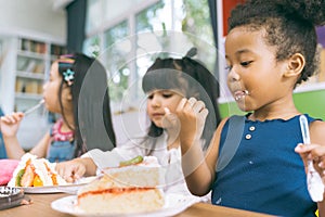 Cute little child girl with diversity friends eating cake together. kids eat dessert.