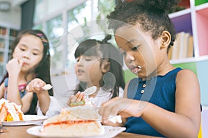 Cute little child girl with diversity friends eating cake together. kids eat dessert.