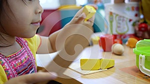 Cute little child girl having fun playing with cooking toys in living room at class room. Kid using wood toy knife slicing vegetab