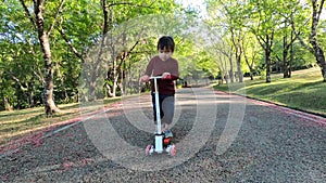 Cute little child girl having fun to riding a scooter on road in a summer park. Concept of happy family and childhood.