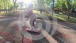 Cute little child girl having fun to riding a scooter on road in a summer park. Concept of happy family and childhood.