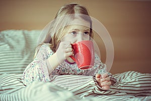 Cute little child girl ill sitting with tea in bed under blancket