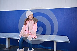 Cute little child girl looking aside, sitting on the banc, waiting for train on the railway station platform