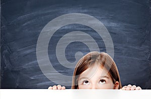 Cute little child girl looking up on the desk at school