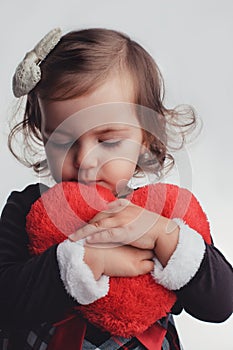 Cute little child girl portrait holding red heart toy on white b