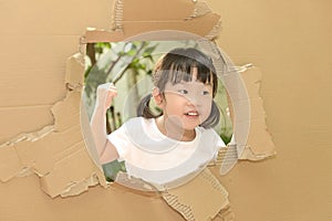 Cute little child girl raising fist in torn paper wall