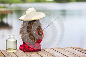 Cute little child girl in rubber boots and straw hat fishing from wooden pier near glass jar and little fish on a lake. Family