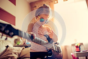 Cute little child girl in sunglasses playing guitar.