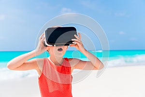 Cute little child girl using VR virtual reality goggles. Adorable girl look into the virtual glasses on white beach