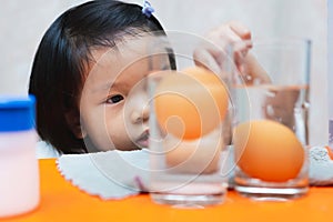 Cute little child girl is wondering about sinking egg-floating egg science experiment.