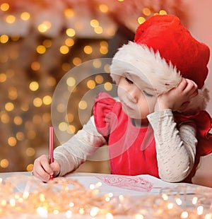 Cute little child girl writes the letter to Santa Claus near Christmas tree indoors.Merry Christmas and Happy Holidays