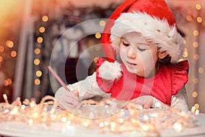 Cute little child girl writes the letter to Santa Claus near Christmas tree indoors.Merry Christmas and Happy Holidays